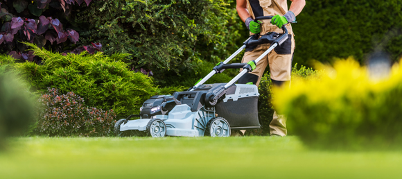 Landscaper using a push mower on a clear day